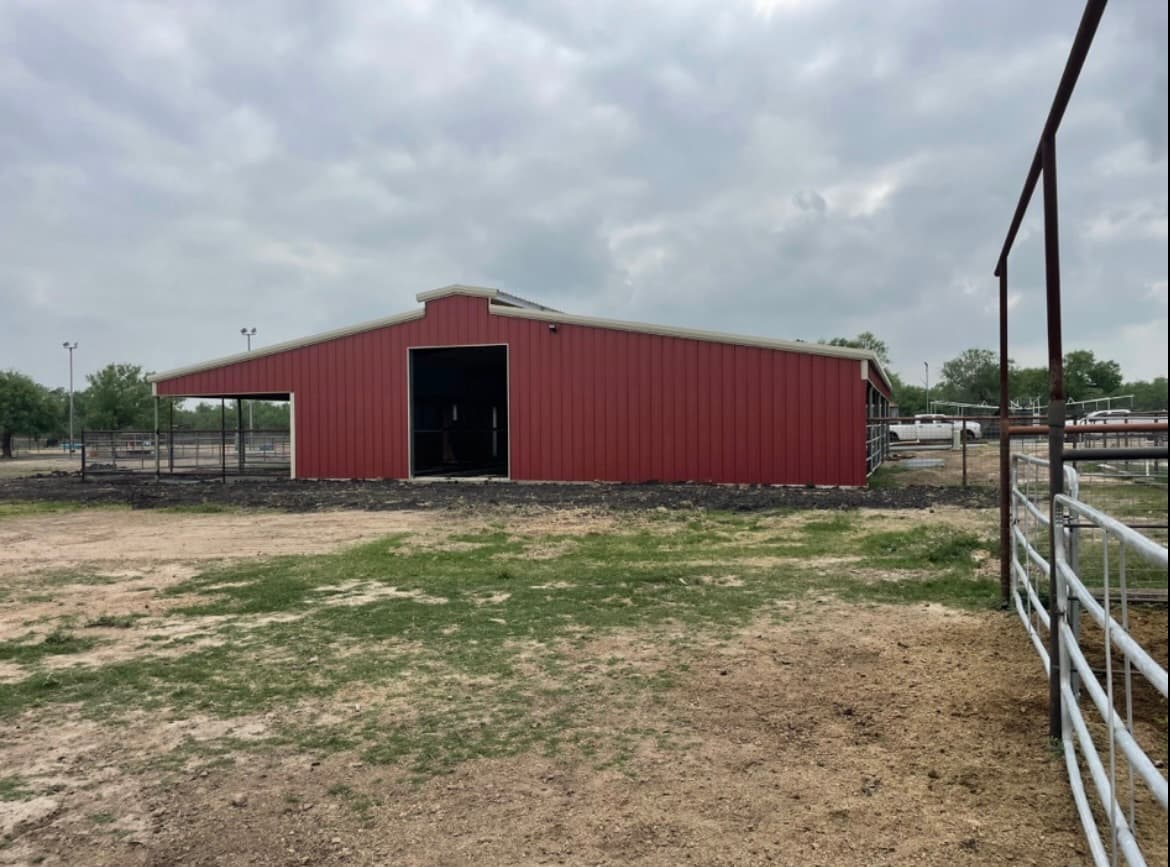 Red metal barn with raised monitor roof, lean-to wings, and adjacent stock pens, South Texas ranch