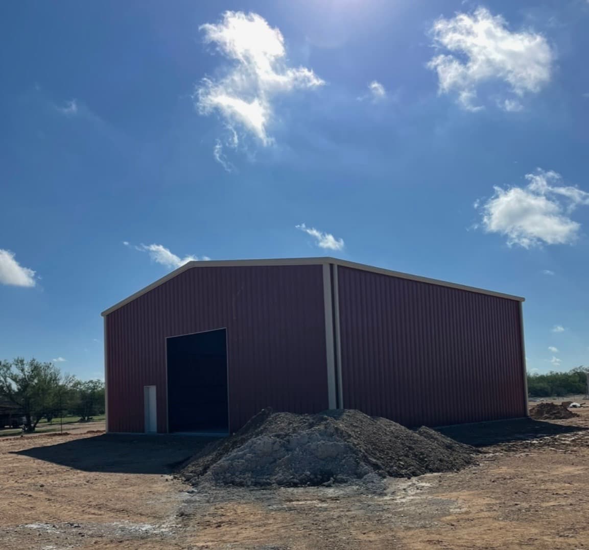 Tall burgundy clear-span warehouse with oversized overhead door for equipment access, South Texas
