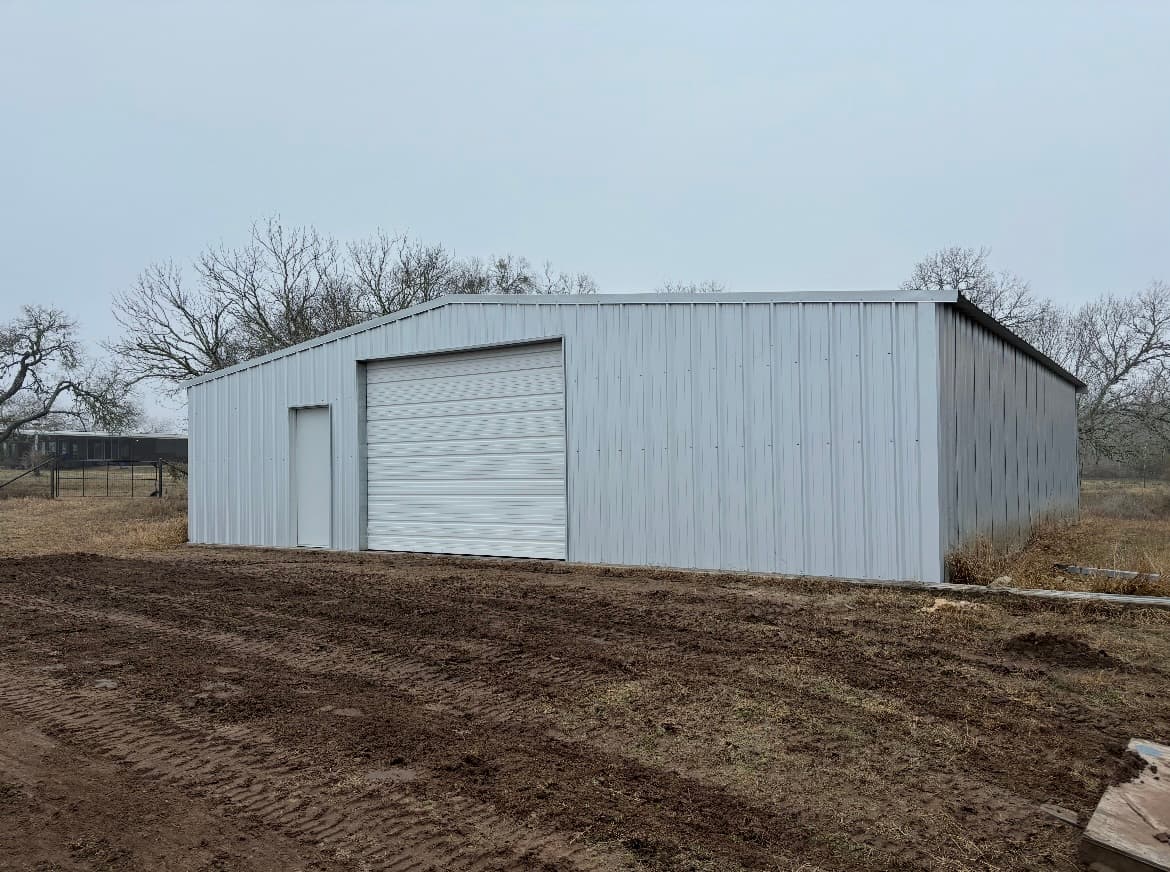 Light grey metal shop building with a single oversized roll-up door and a walk door, South Texas